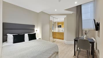 Una habitación de hotel moderna con una cama grande, un escritorio con una silla y vistas a la cocina y el comedor.