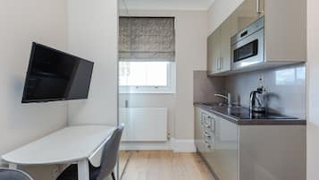 A modern kitchen with a built-in oven, microwave, and kettle. There is a dining table with chairs and a TV mounted on the wall.