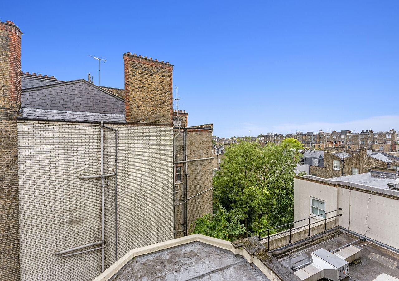 Eine Dachterrasse mit Backsteinmauer, Metallgeländern und einem Baum.