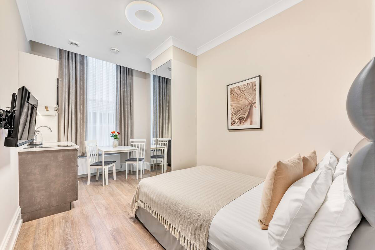 A hotel room with a bed, a desk with a chair, a television, and a window with curtains.