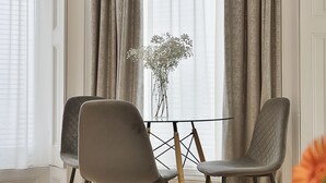 A room with a table and two chairs, a vase with flowers, and a view through sheer curtains. - Cleveland Residences Kensington (London)