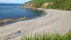 A coastal beach with a clear sky, a grassy hill, and a tent on the sand. - The Fish Cellars - Luxury Holiday Cottage (Portwrinkle)