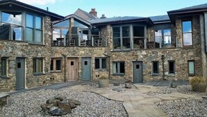 A stone building with multiple windows and doors, a balcony, and a gravel courtyard. - The Fish Cellars - Luxury Holiday Cottage (Portwrinkle)