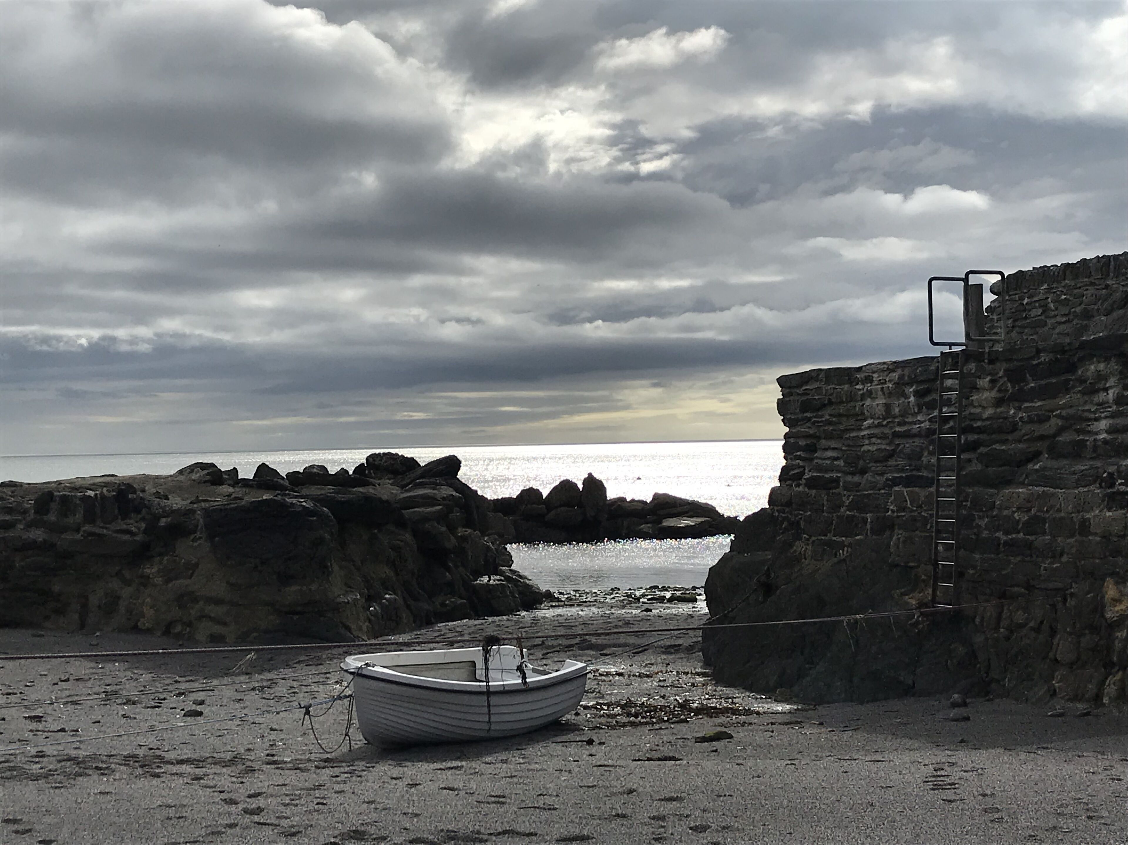 A boat on a rocky beach with a stone wall and a ladder.