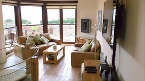 A spacious living room with a high ceiling, large windows, and a balcony. - The Fish Cellars - Luxury Holiday Cottage (Portwrinkle)