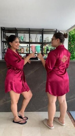 Two individuals in matching pink robes standing in a room with a tiled floor and a shelf with various bottles in the background. - The View Hostel & Lounge (Cali)