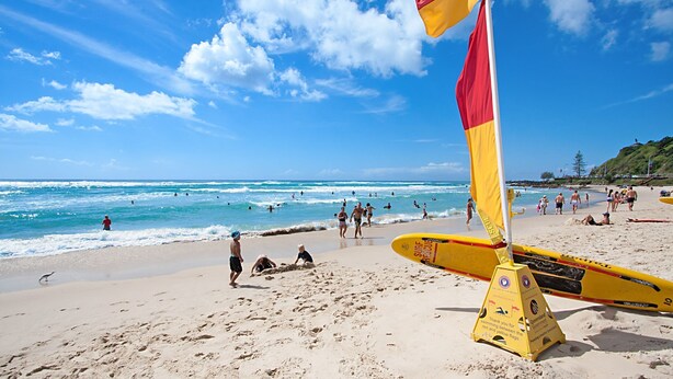 A beach with people swimming and walking, a lifeguard stand, and a clear blue sky. - 3 Haig Place - 100m from Kirra Beach with Wi-Fi included (Coolangatta)