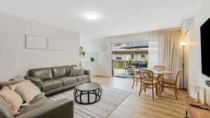 A modern living room with a leather sofa, a round coffee table, and a dining area with wicker chairs and a glass table. - 3 Haig Place - 100m from Kirra Beach with Wi-Fi included (Coolangatta)