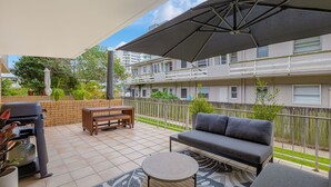 A balcony with a grill, a sofa, a table, and a large umbrella. - 3 Haig Place - 100m from Kirra Beach with Wi-Fi included (Coolangatta)