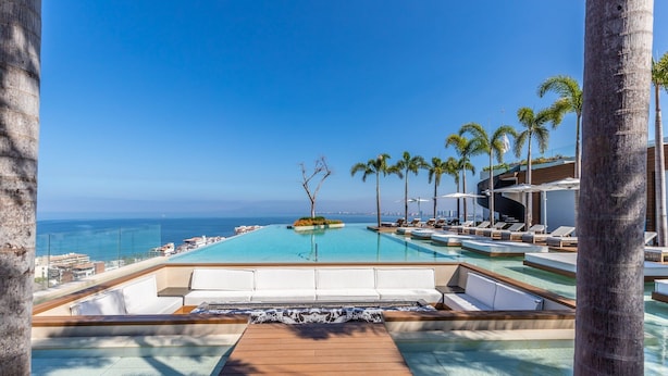 Un área de piscina en un resort con terraza de madera, sillas reclinables y palmeras.