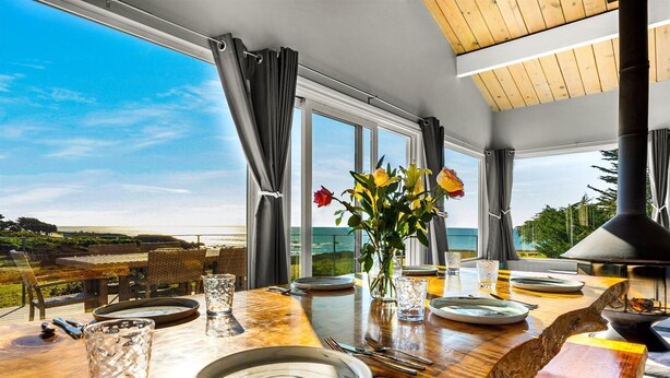 Un comedor con una mesa dispuesta para dos, un florero con flores y vista al océano.