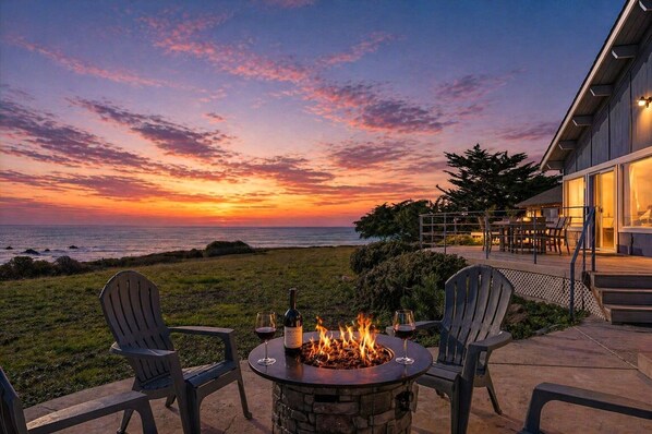 A patio with a fire pit, two chairs, and a bottle of wine.