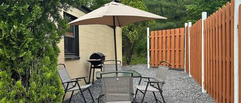 An outdoor patio with a table and chairs, surrounded by a gravel path and a wooden fence.