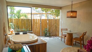 A bathroom with a bathtub, wooden furniture, a round table, and a view of the outside. - Pousada Mansão da Costa (Maragogi)