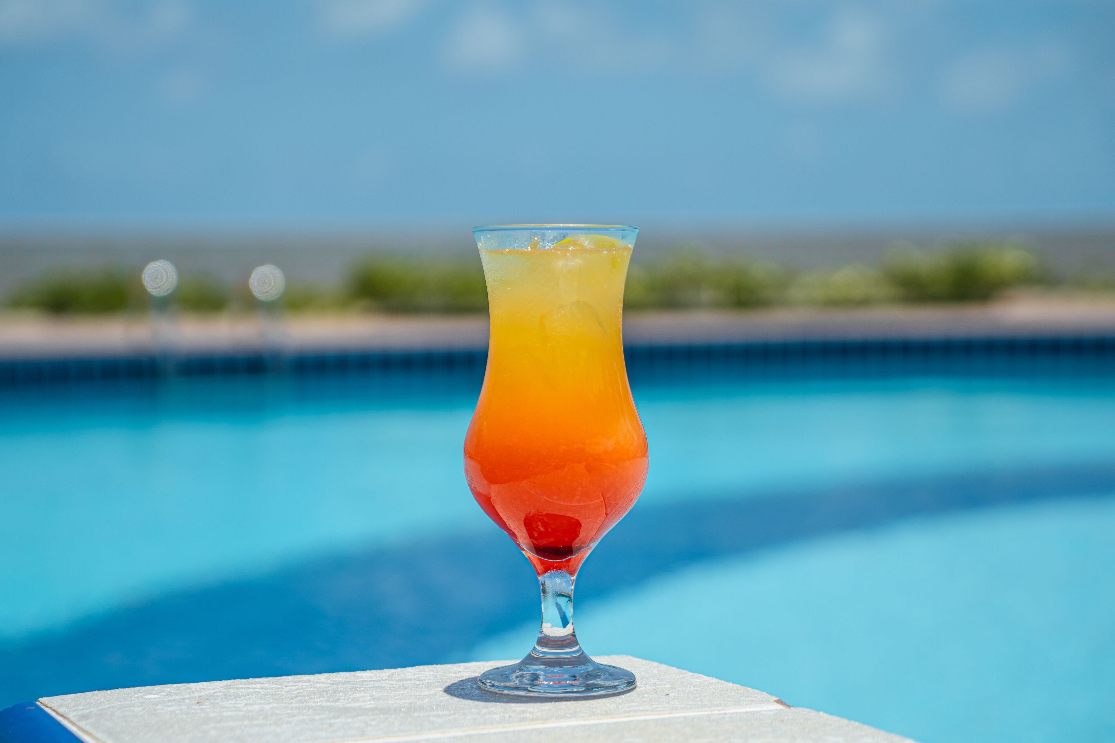 Ein Cocktailglas mit einem geschichteten Getränk auf einem Tisch am Pool.