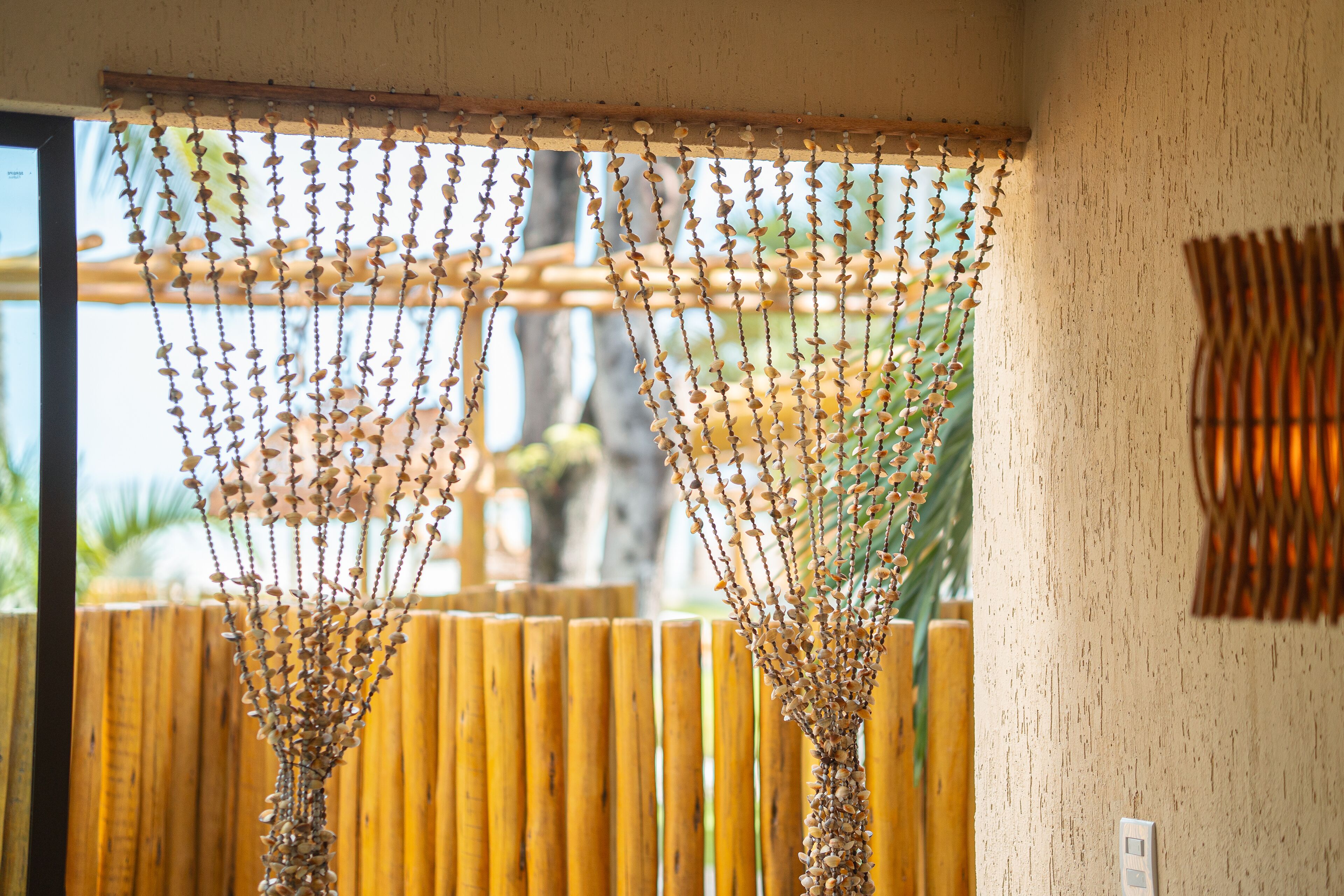 A room with a wooden fence, a decorative hanging with small beads, and a wall-mounted light switch.