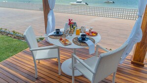 A dining table with chairs on a wooden deck overlooking a beach with boats. - Pousada Mansão da Costa (Maragogi)