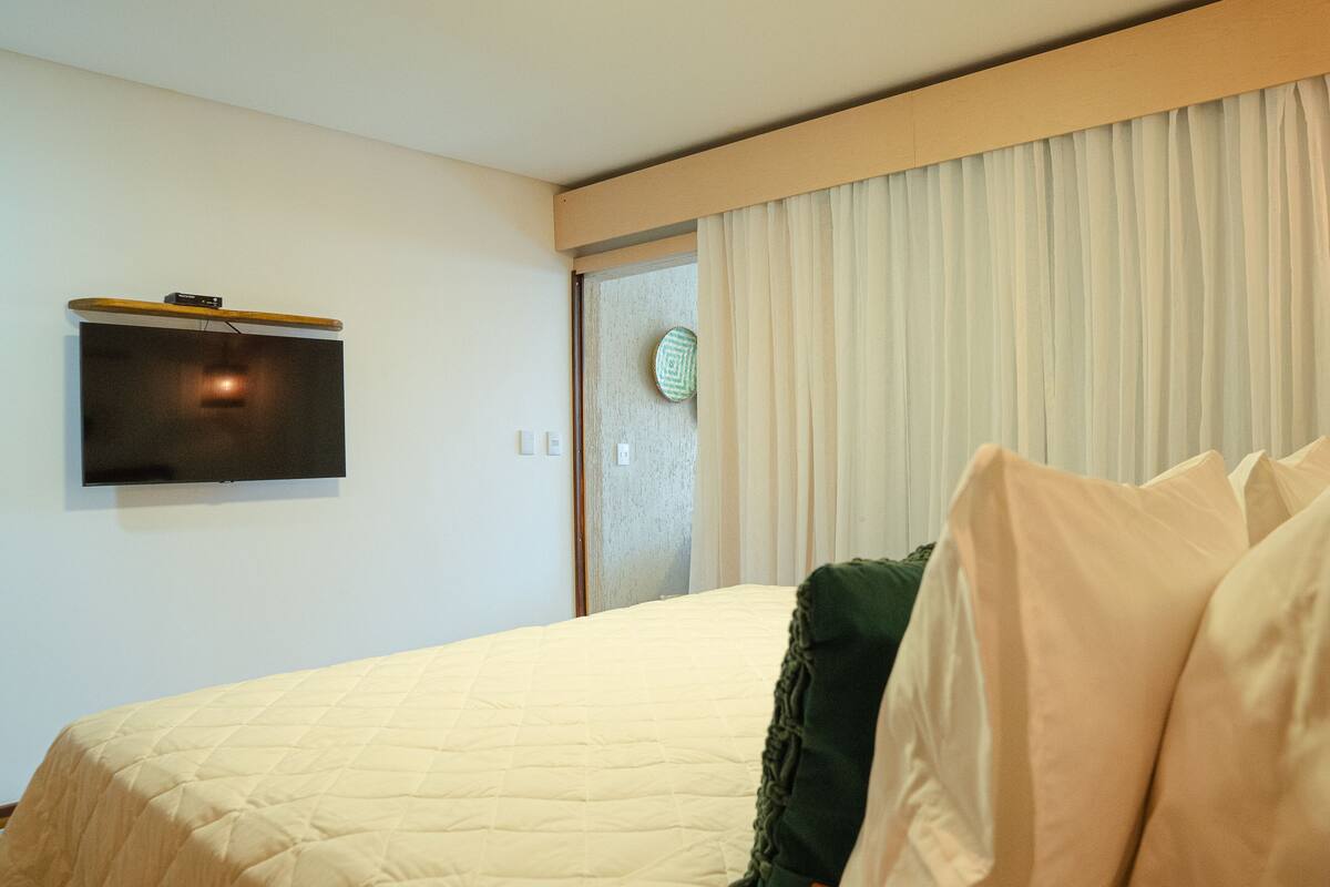 Ein Hotelzimmer mit Bett, Wandfernseher und einer Tür mit Vorhang.