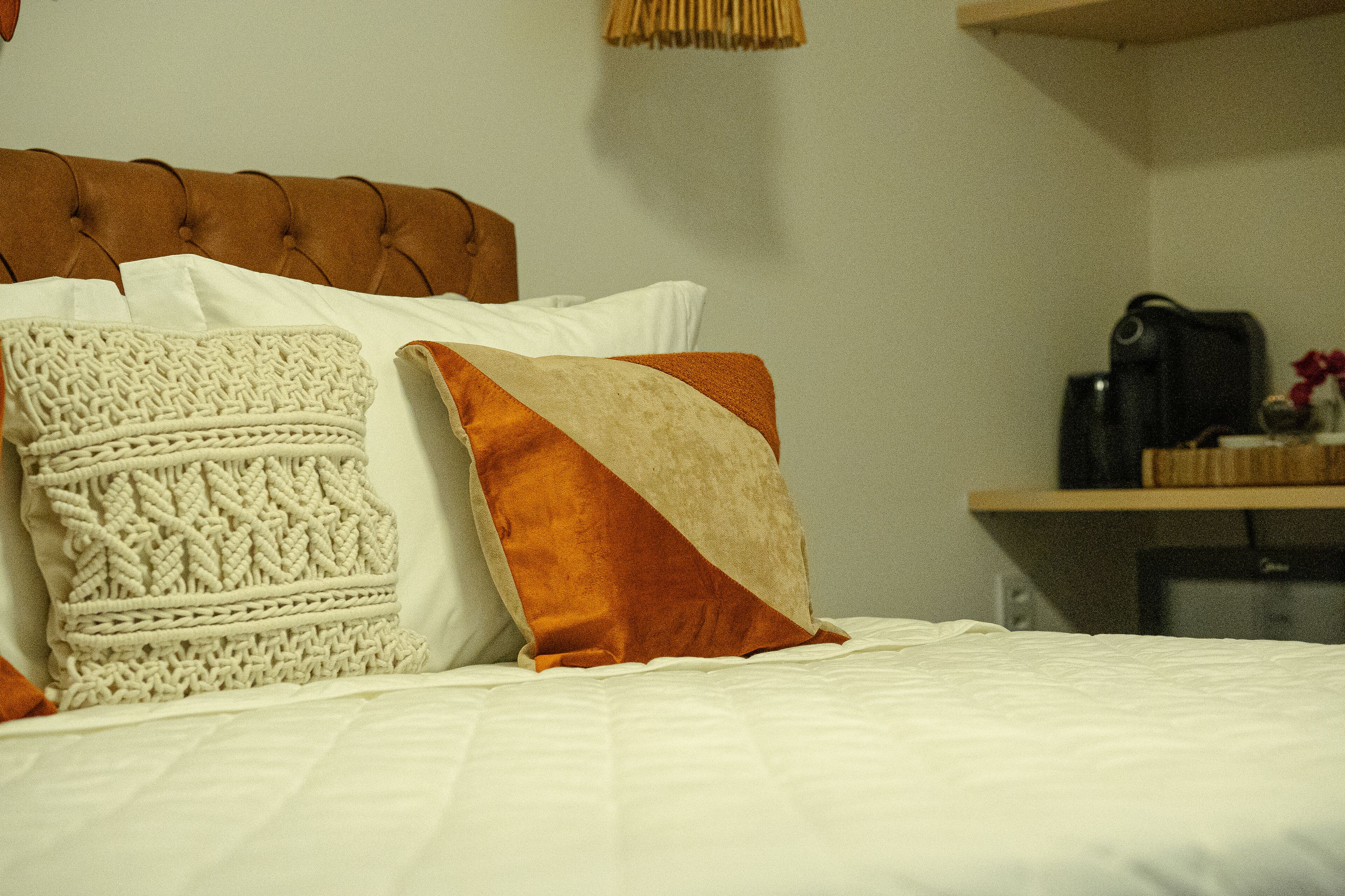 Un lit avec une tête de lit capitonnée, du linge de lit blanc et des coussins décoratifs.
