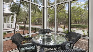 A glass-enclosed porch with wicker furniture and a view of a landscaped area with trees and a pathway.