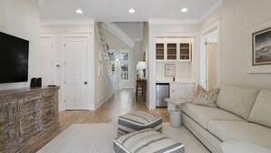 A spacious living room with a large flat-screen TV, a wooden cabinet, a sofa, and a staircase leading to another room. - Close to Parks with Private Pool and Bikes (Santa Rosa Beach)