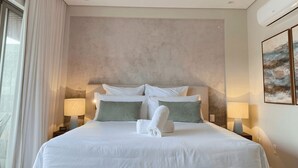 Een hotelkamer met een groot bed, twee bedlampen, een wandairconditioner en een raam met gordijnen.
