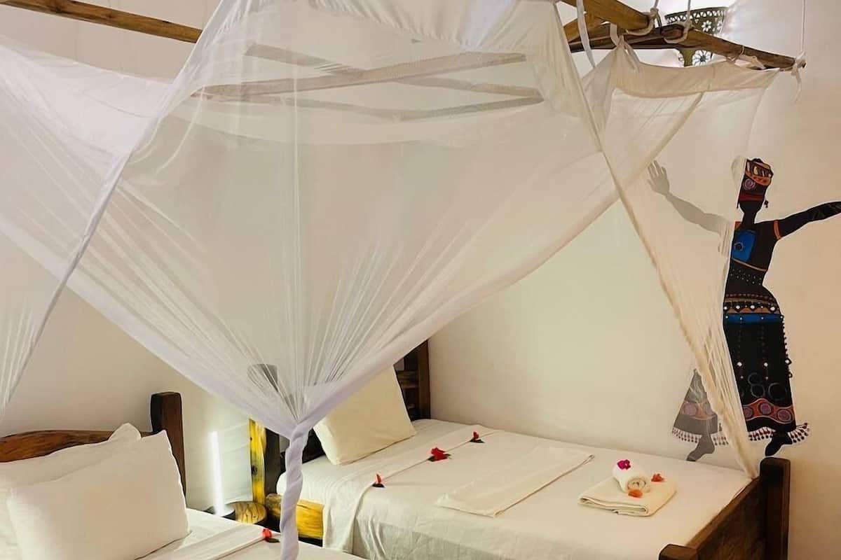 A room with two wooden beds, each with a canopy bedspread and rose petals.