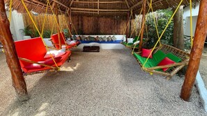 A covered outdoor seating area with red and green hammocks, a white sofa with cushions, and a bamboo wall. - Babalao Bungalows (Nungwi)