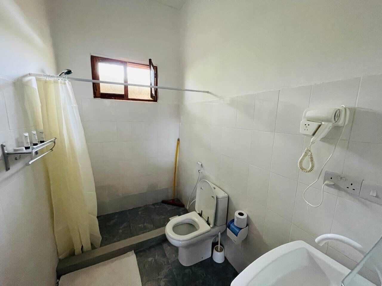 Un baño pequeño con inodoro, ducha, ventana y teléfono.