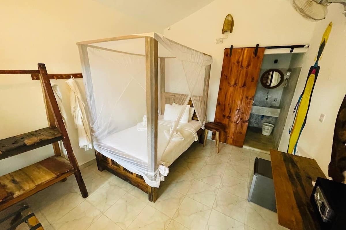 A room with a four-poster bed, wooden furniture, and a small bathroom area.