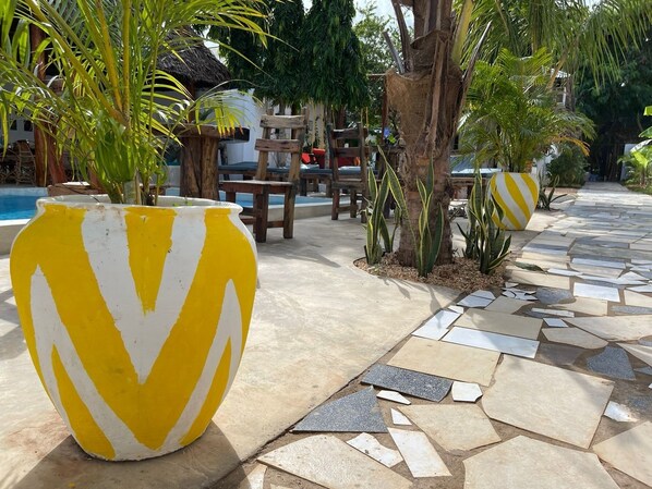 A patio area with a stone-tiled floor, large yellow and white planters, and a thatched-roof structure in the background. - Babalao Bungalows (Nungwi)