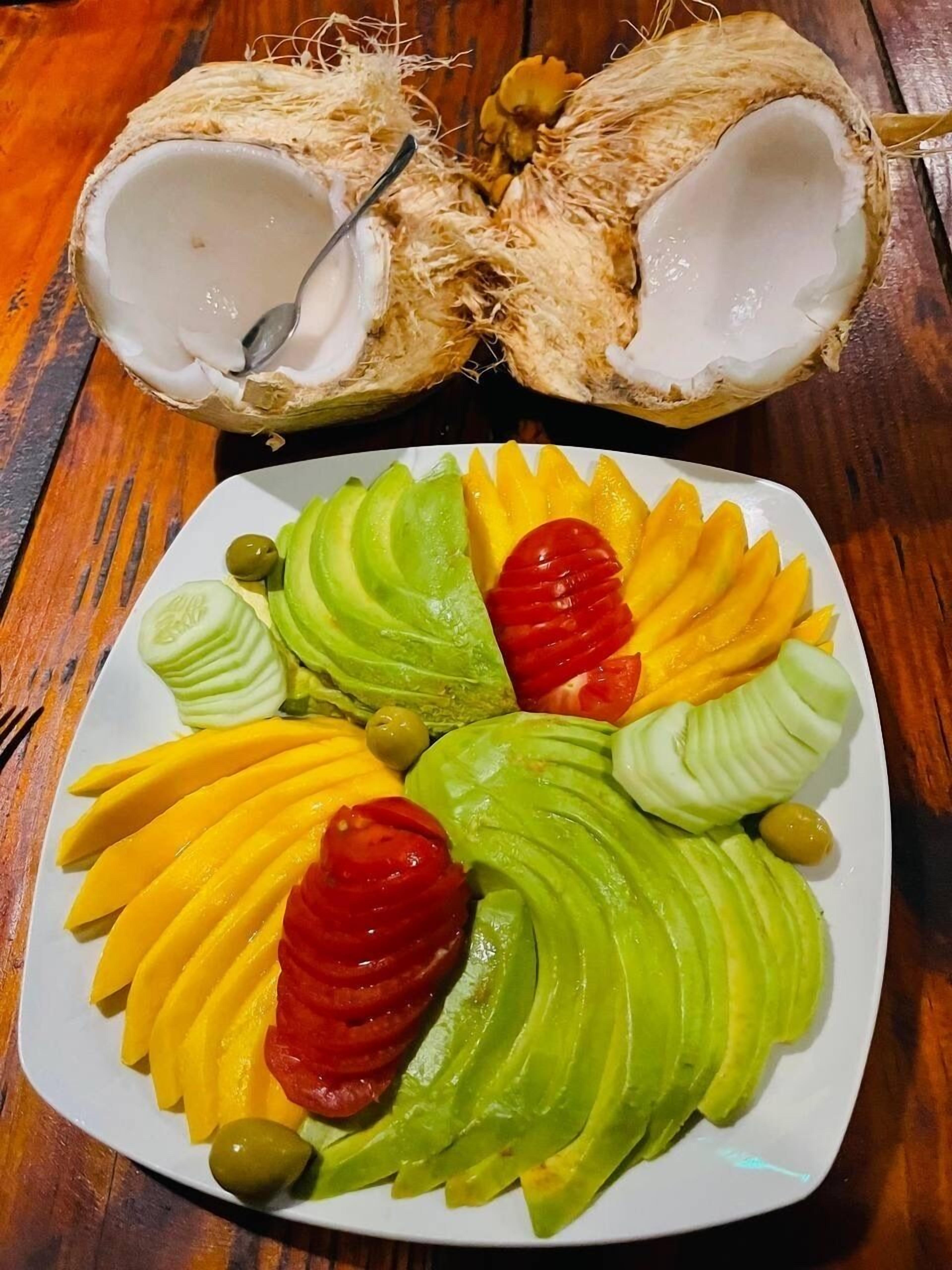 A plate of sliced fruits and a half coconut with a spoon.