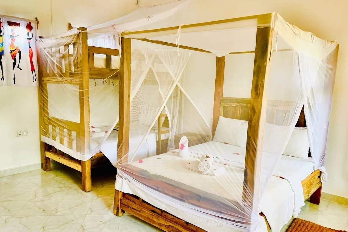 Two wooden beds with white bedding and mosquito netting, a tiled floor, and a wall with a decorative panel.