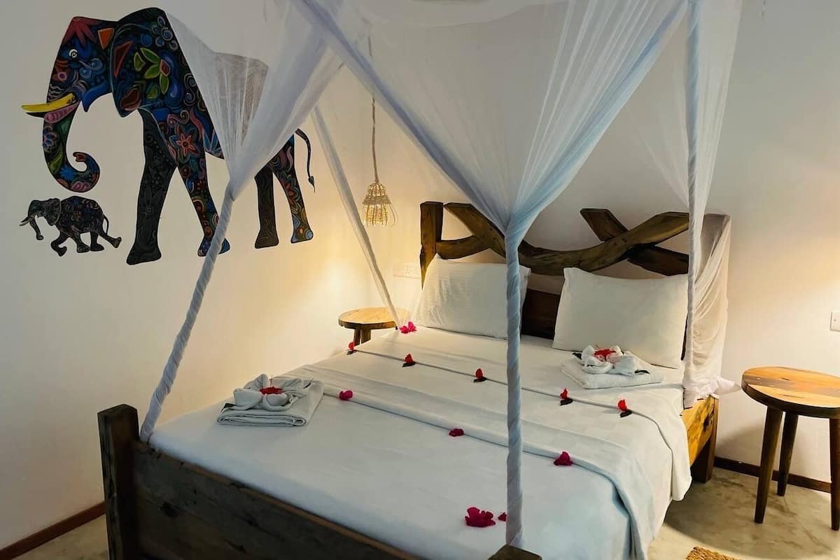 A bed with a canopy, a wall mural of an elephant, and a small round table.