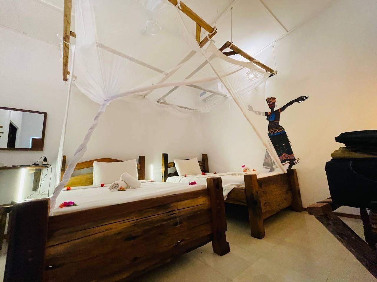 Een kamer met twee houten bedden, een klamboe en een decoratief object aan de muur.