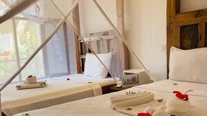 A room with two beds, each with white linens and pillows, a wooden headboard, and a small bedside table with a radio. - Babalao Bungalows (Nungwi)