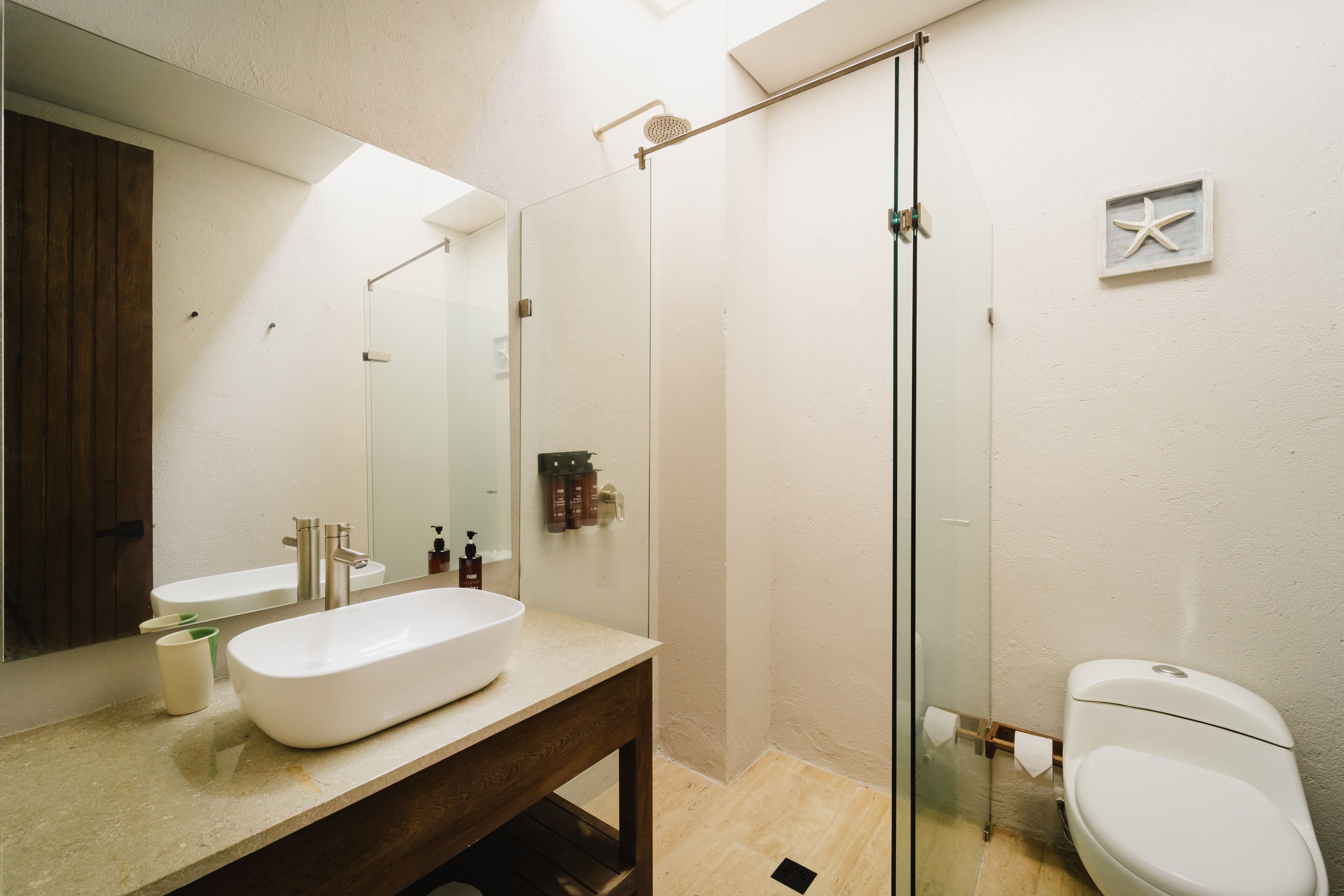 Un baño moderno con un espejo grande, un lavabo blanco y una cabina de ducha con mampara de vidrio.
