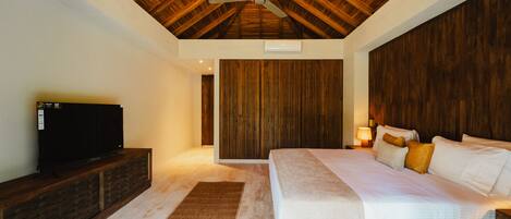 Un dormitorio con techo de madera, una cama con ropa blanca, un televisor sobre un mueble de madera y un panel de pared de madera.
