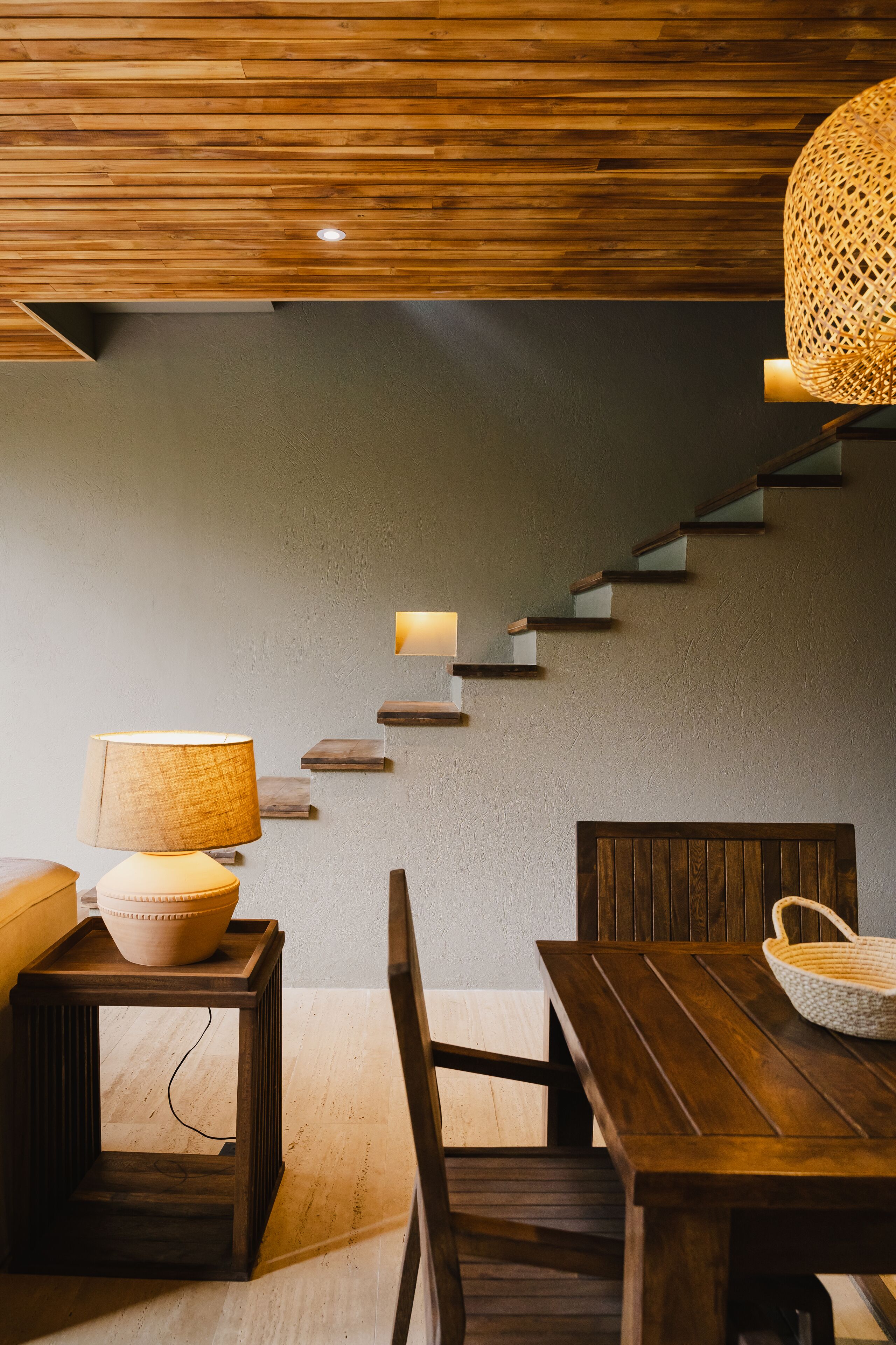 A wooden staircase with built-in lighting, a dining table with chairs, and a hanging light fixture.