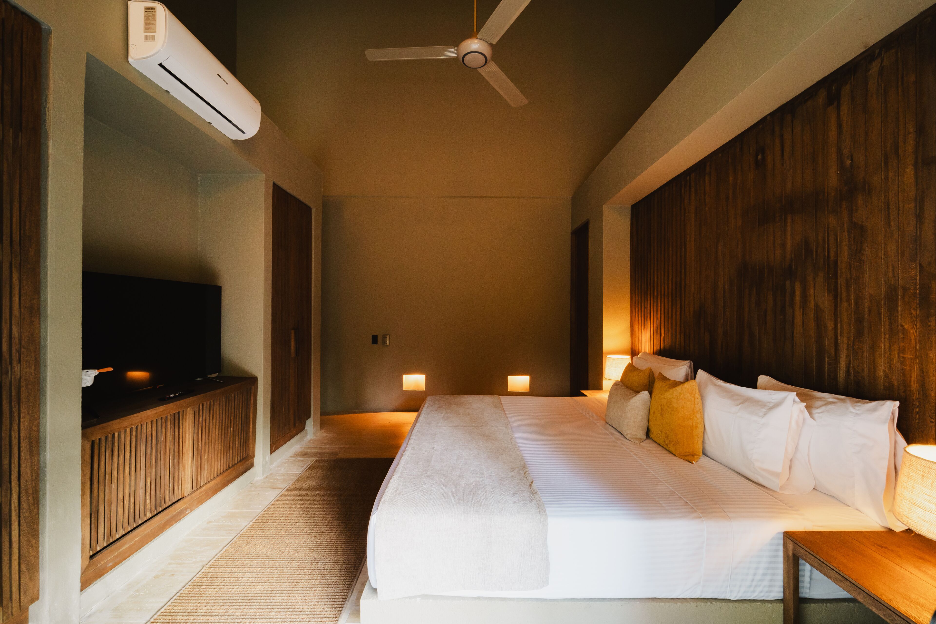 A hotel room with a bed, a TV, a ceiling fan, and two bedside lamps.