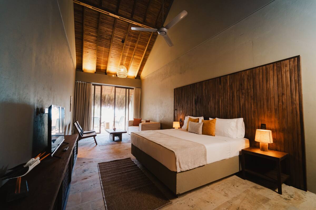 A spacious bedroom with a large bed, a ceiling fan, a TV, and a seating area with a table and chairs.