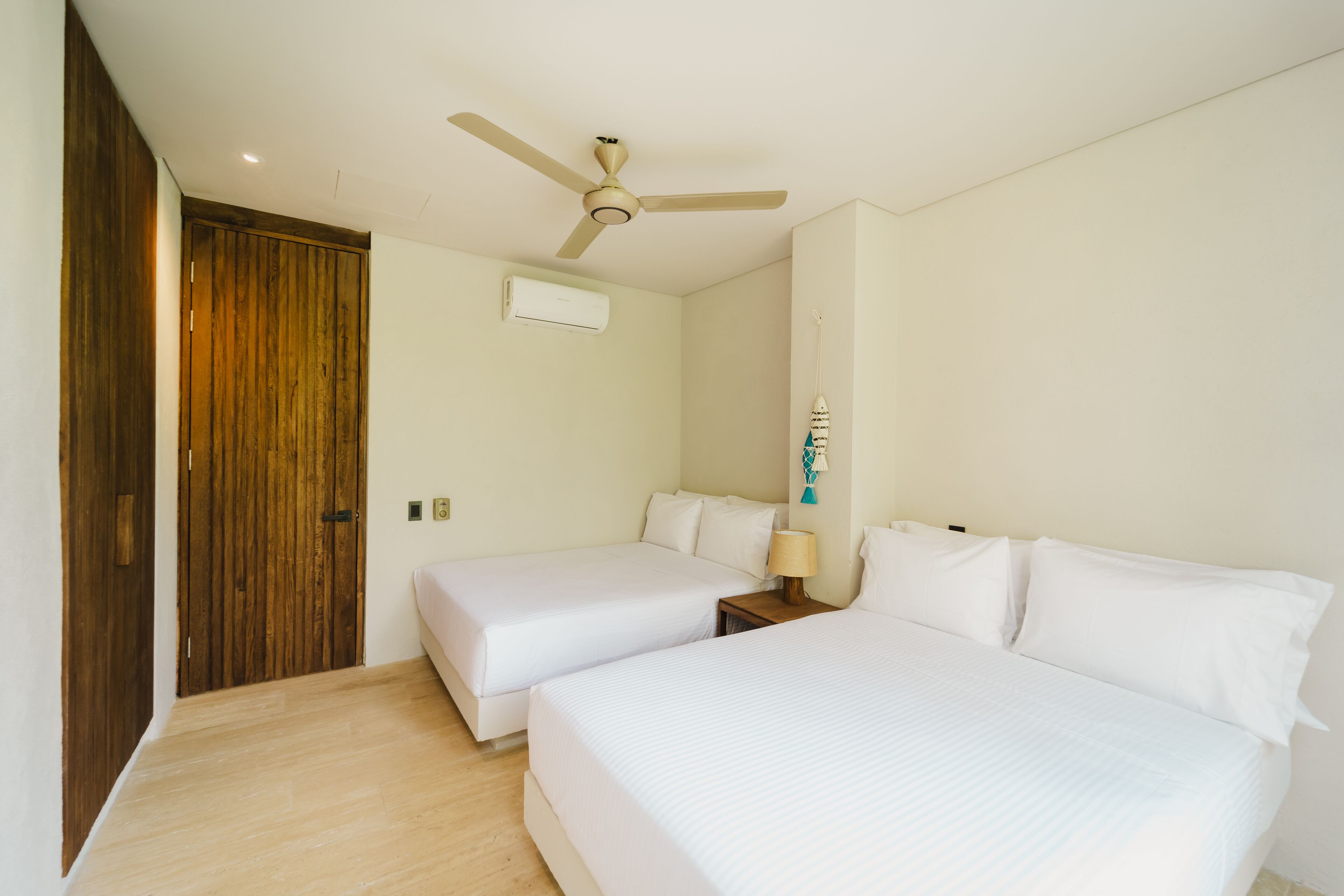Una habitación de hotel con dos camas individuales, un ventilador de techo, un equipo de aire acondicionado y una puerta de madera.