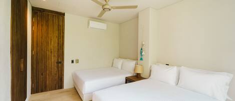 Una habitación de hotel con dos camas individuales, un ventilador de techo, un equipo de aire acondicionado y una puerta de madera.