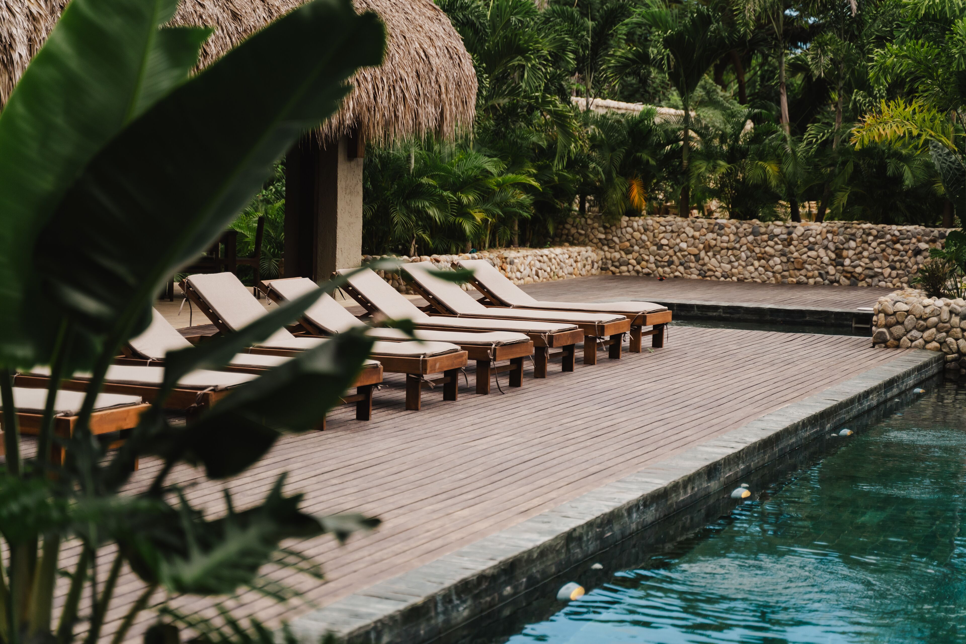 Una terraza de madera con sillones de descanso y una piscina.