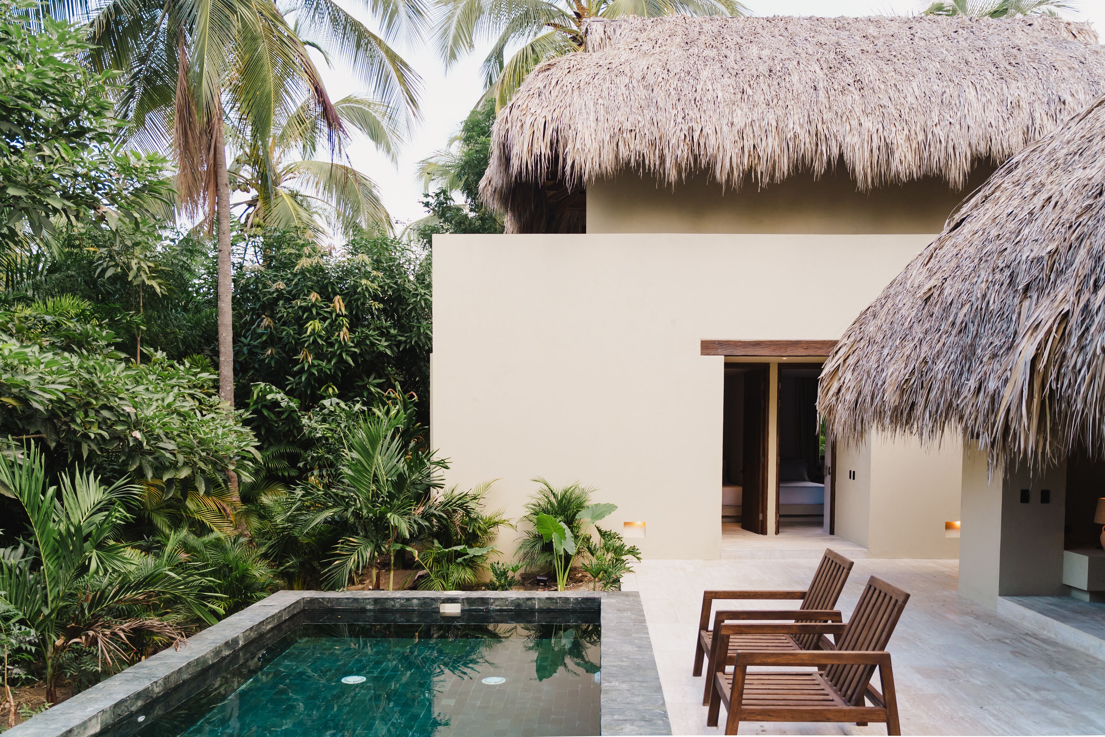 A poolside area with a thatched-roof structure, surrounded by lush tropical vegetation.