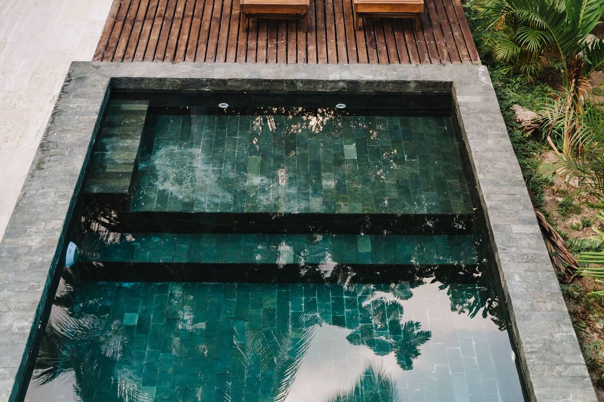A rectangular pool with wooden deck seating and lush greenery in the background.