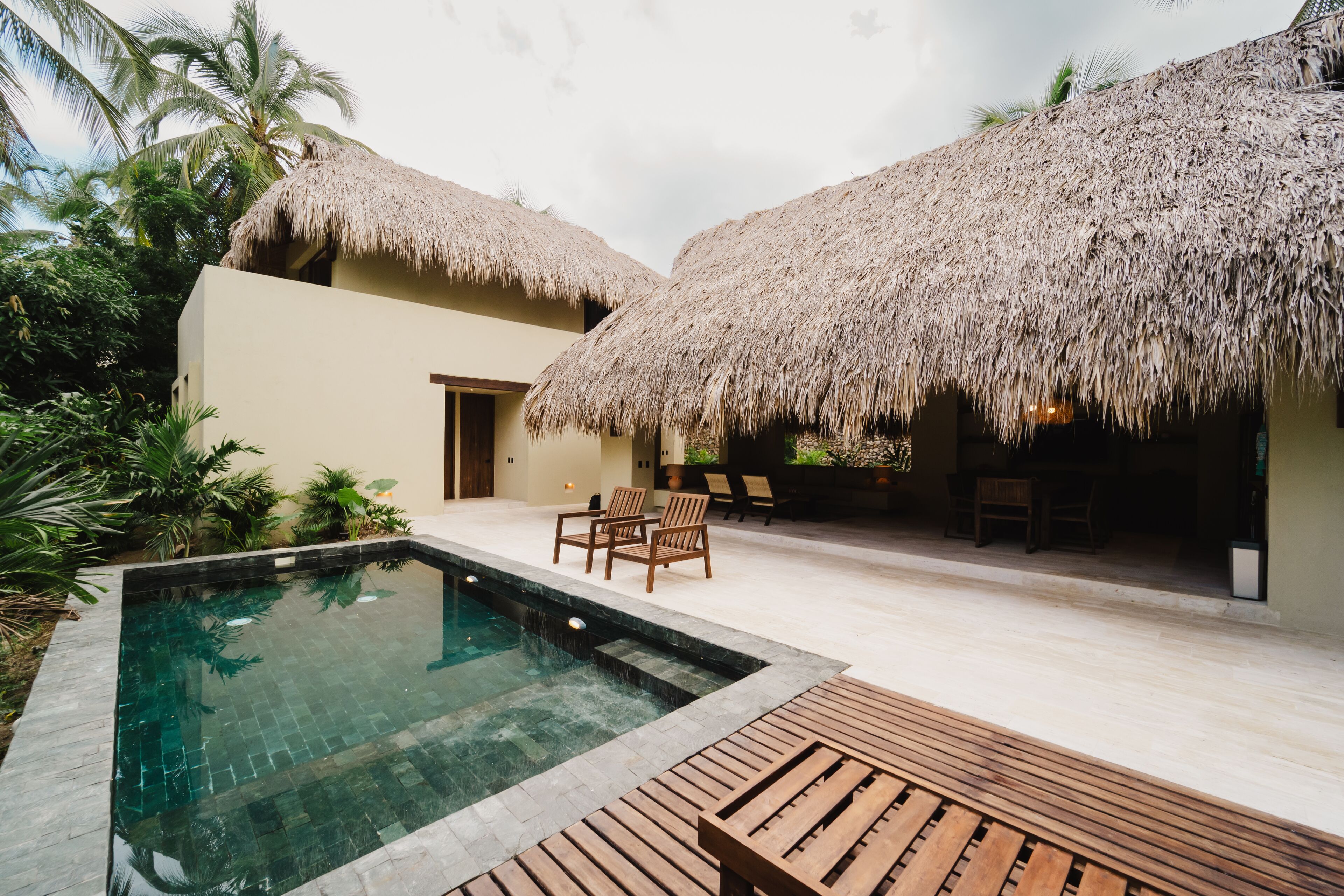 A pool area with a thatched-roof structure, wooden deck, and outdoor seating.