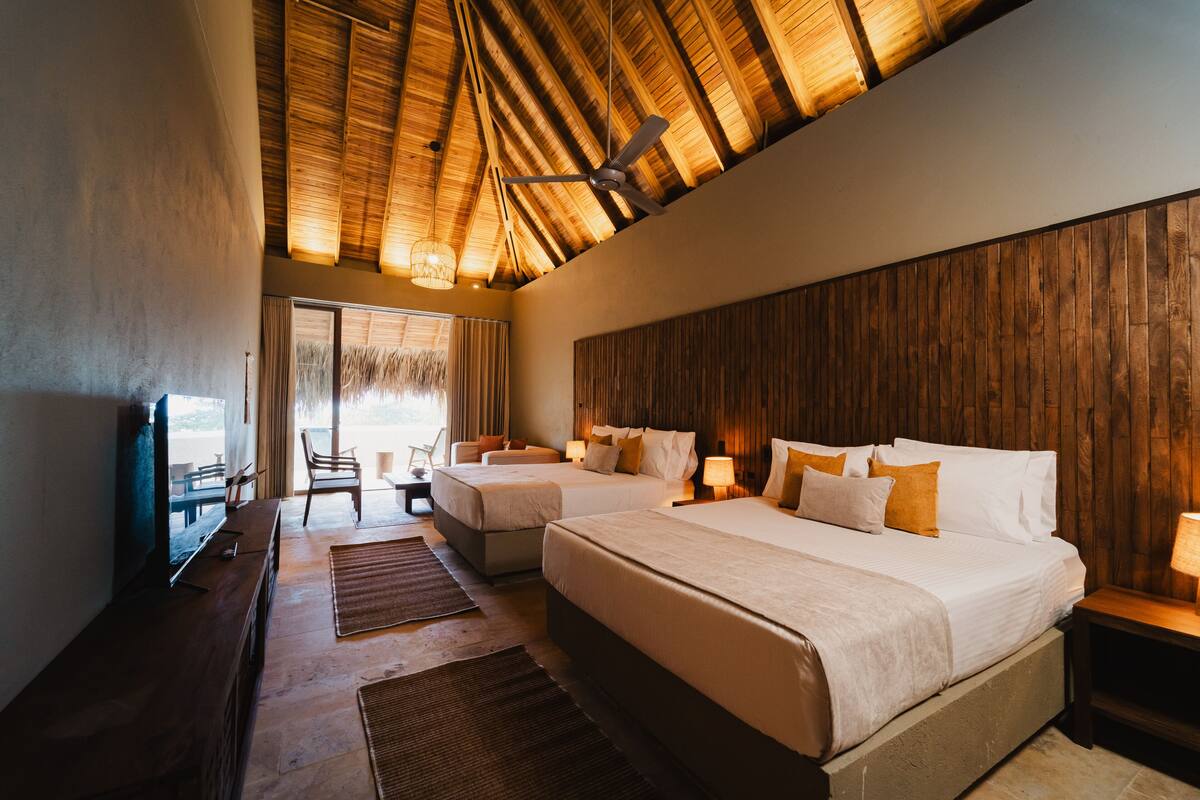 A hotel room with two beds, wooden ceiling, and a large window with a view.