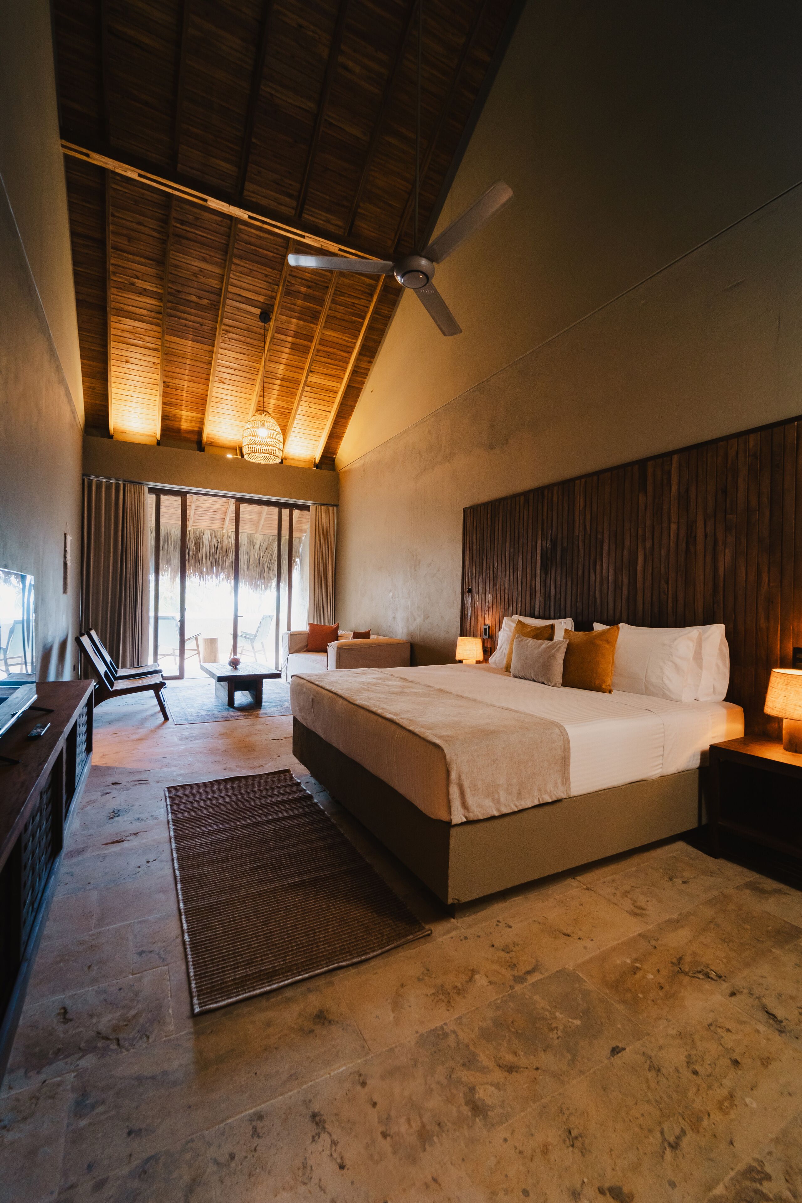 A spacious bedroom with a large bed, a ceiling fan, and a view of the outdoors through a sliding door.