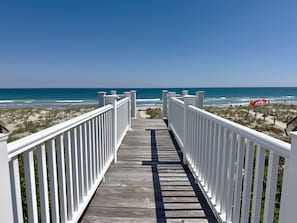 A wooden boardwalk leading to a beach with white railings.
